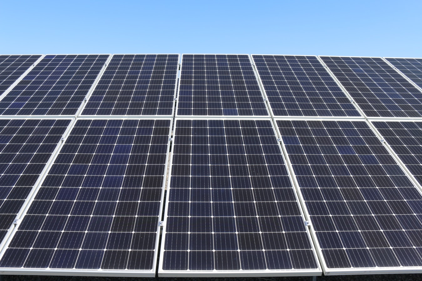 Multiple solar panels fastened together, underneath a clear blue sky.