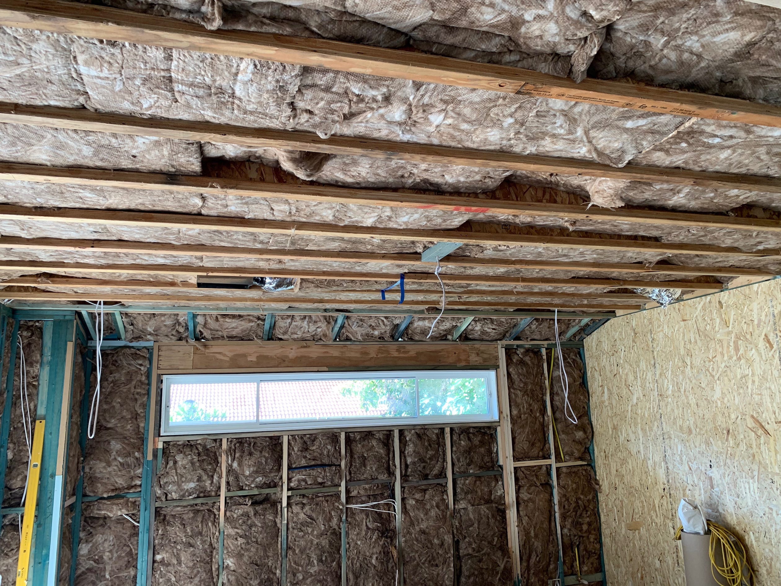A photo of the insulation within a wall and a portion of the ceiliing, placed in between wooden beams.